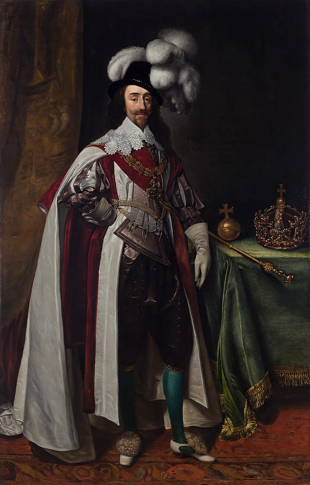 Full-length painting of Charles I wearing red, velvet robes and a hat with large, white feathers. He is leaning against a table. On it is a crown, orb and sceptre.